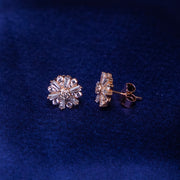 A pair of sterling silver earrings with a rose gold color finish, featuring floral embellishments on a blue background.